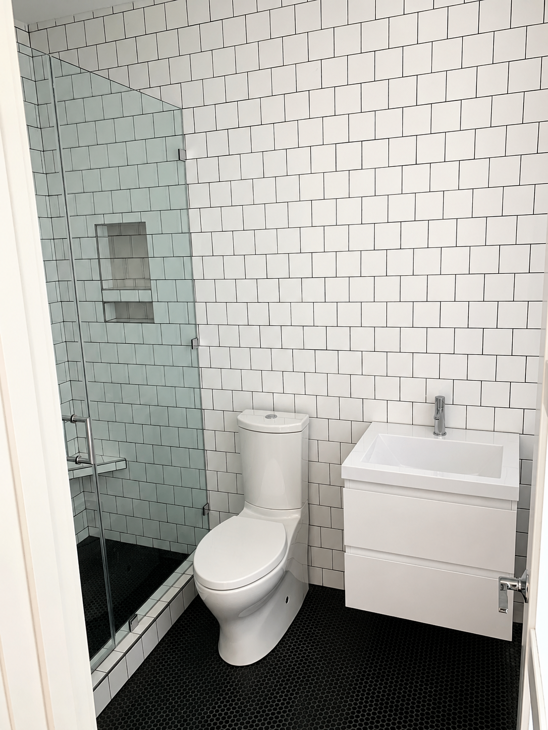 Modern bathroom with white subway tile walls, black hex floor tile, floating vanity, and glass shower