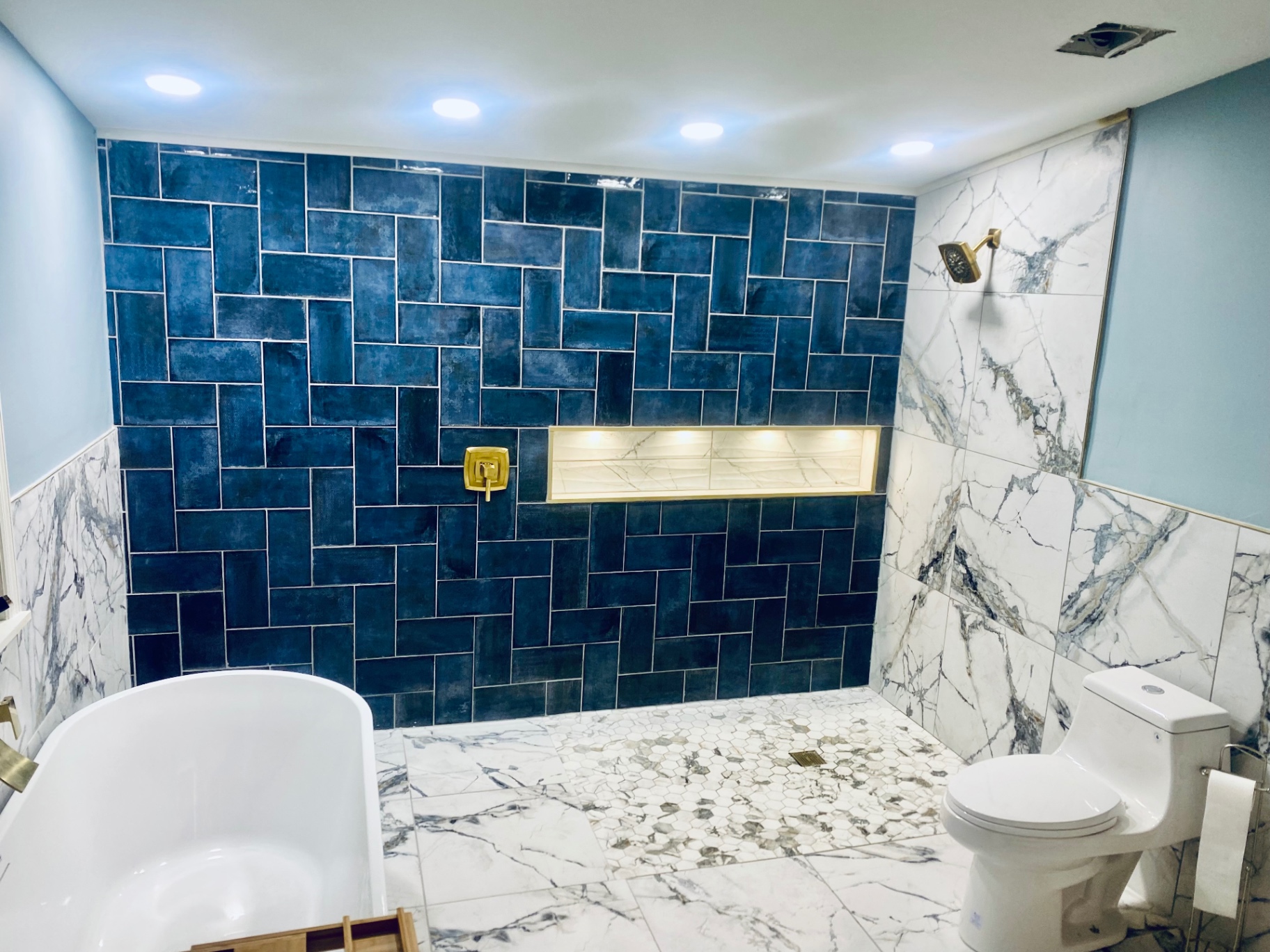 Luxury bathroom with deep blue herringbone tile, marble surround, and brushed gold fixtures