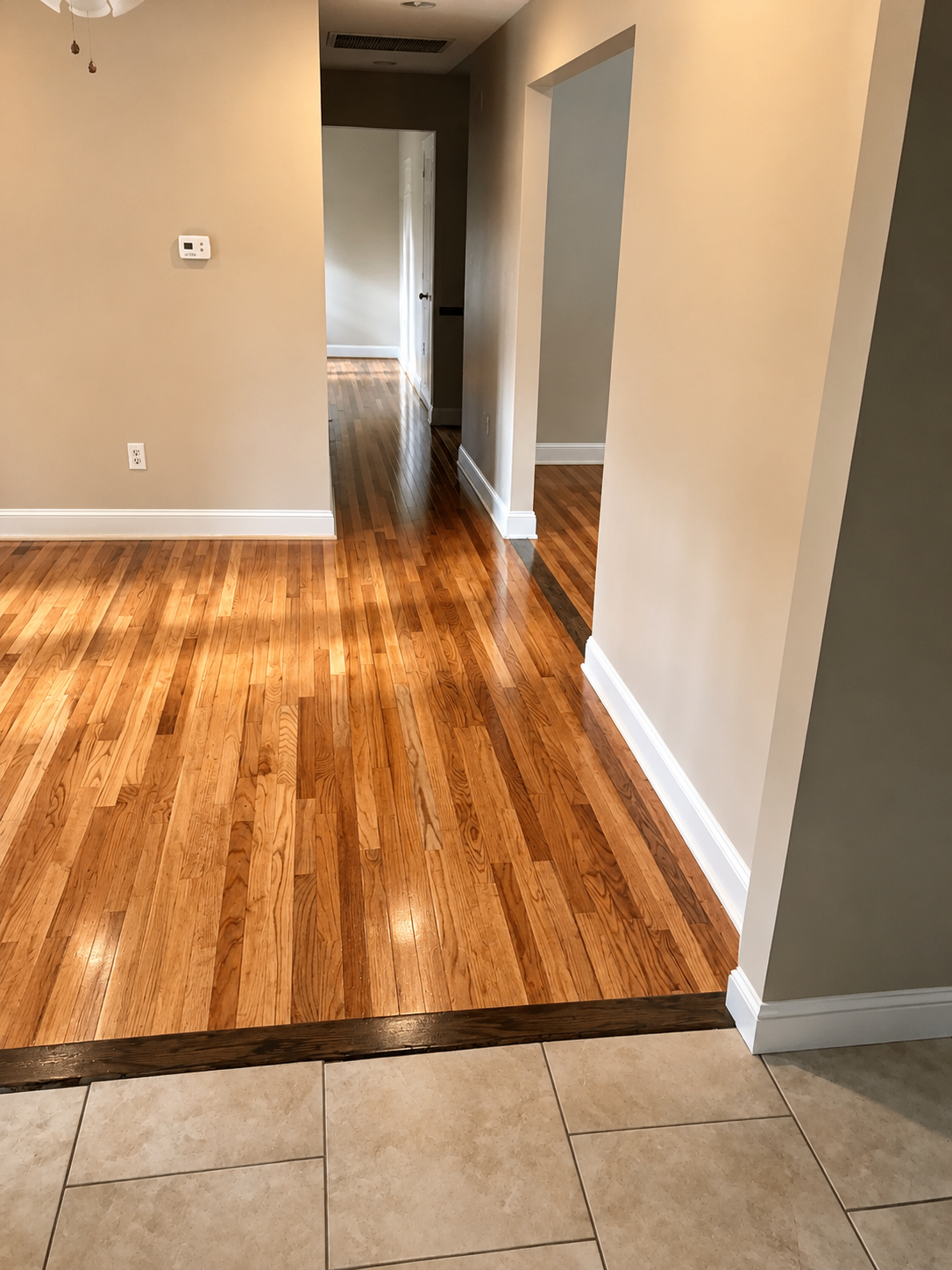 Refinished red oak hardwood flooring transitioning to tile in an open hallway