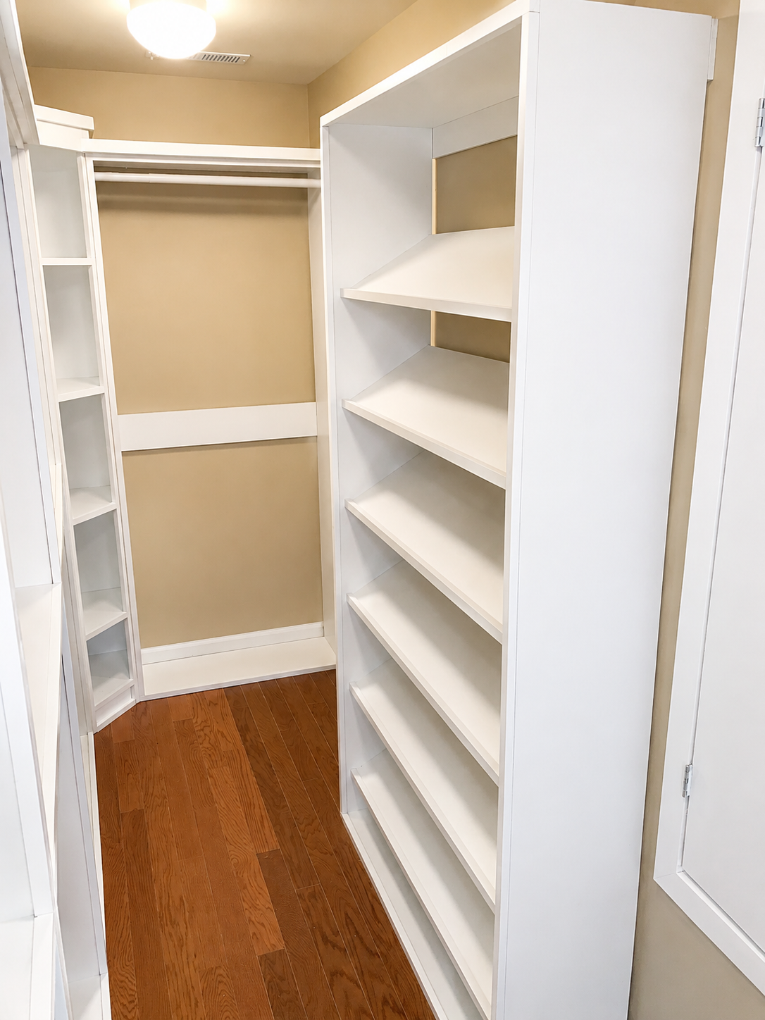 Walk-in closet with white built-in shelving tower, hanging rods, and hardwood floors