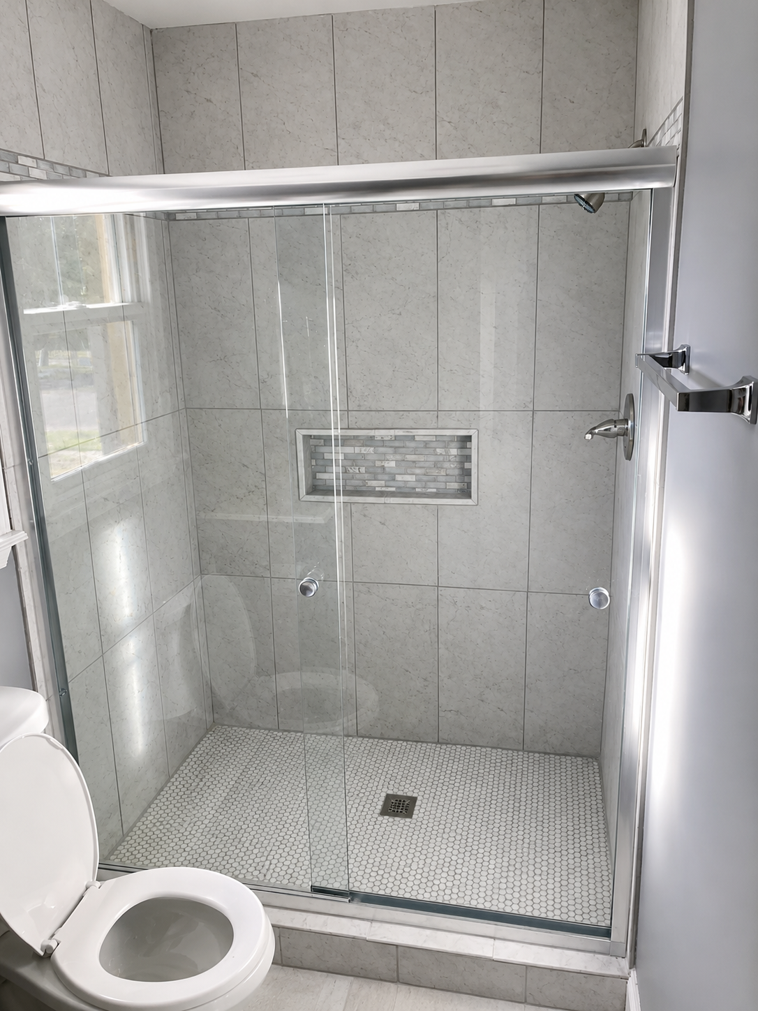 Frameless glass shower enclosure with large-format Carrara-look tile, mosaic accent, and penny-round floor