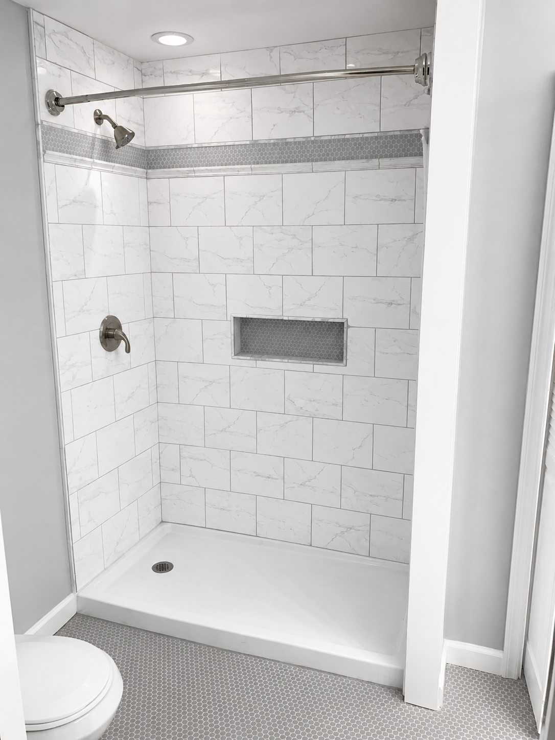 Marble-look tile shower with hexagon mosaic accent stripe, built-in niche, and grey penny-round floor tile