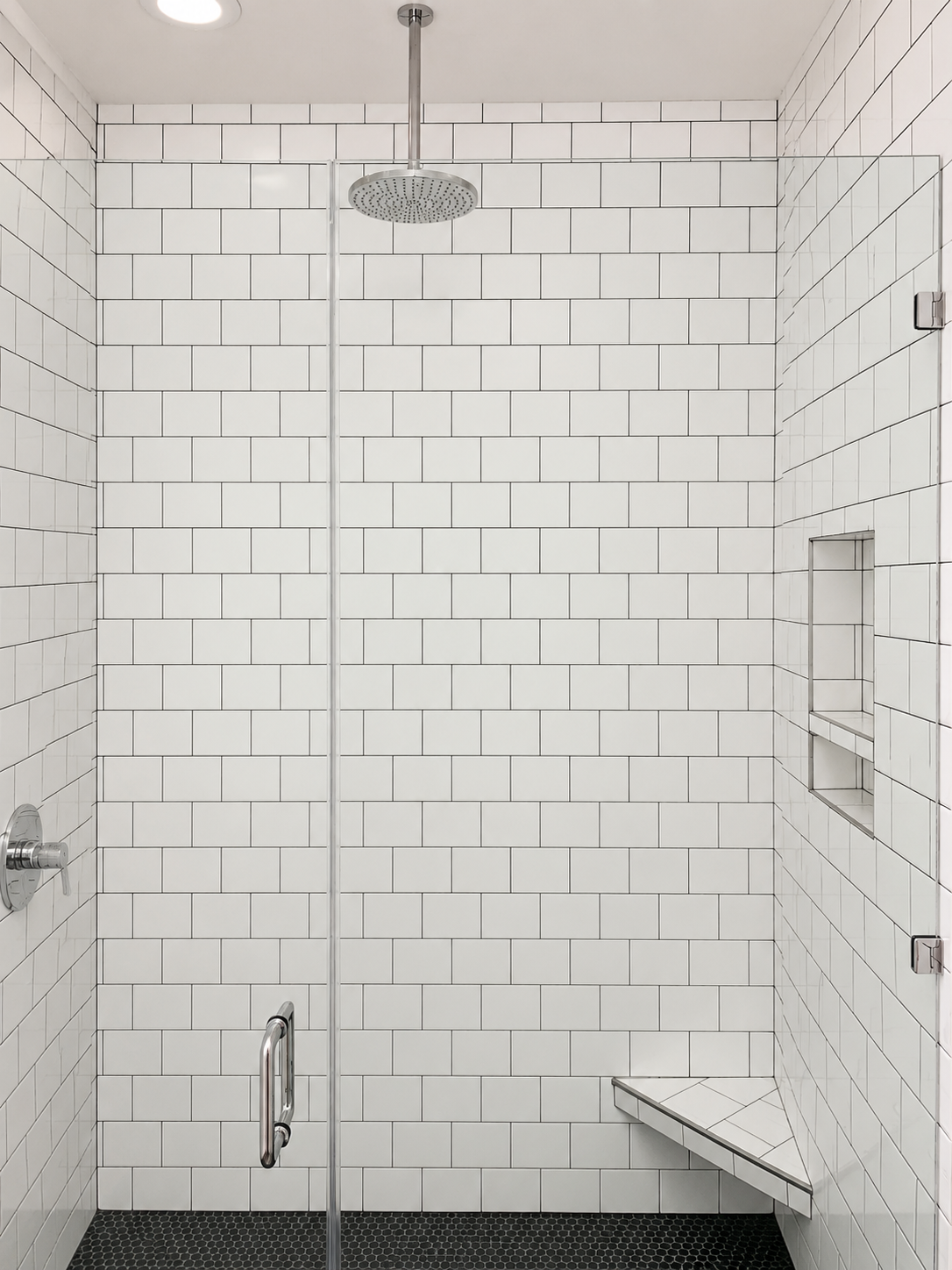 Walk-in subway tile shower with rainhead fixture, corner bench, built-in niches, and black hex floor tile